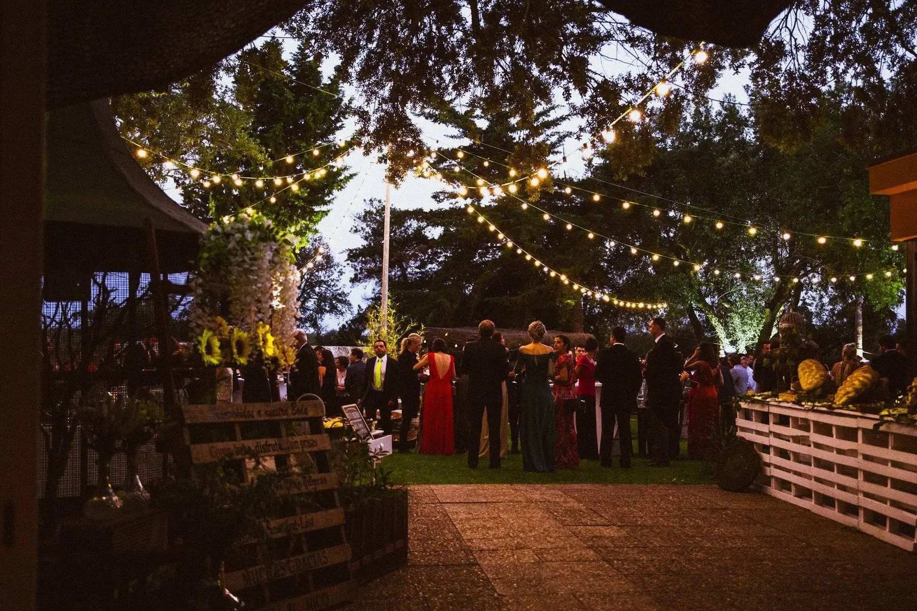 Los invitados bajo guirnaldas de luces en el jardín, con una pared de palés a la derecha