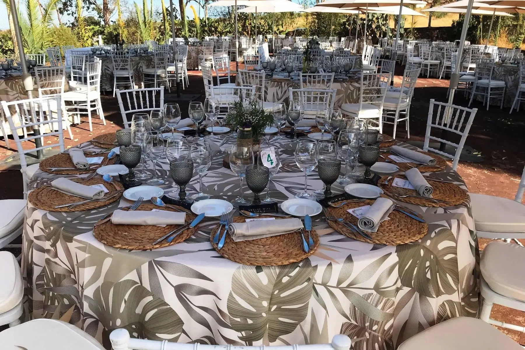 A round table with a leaf-print cloth, esparto placemats and white chairs