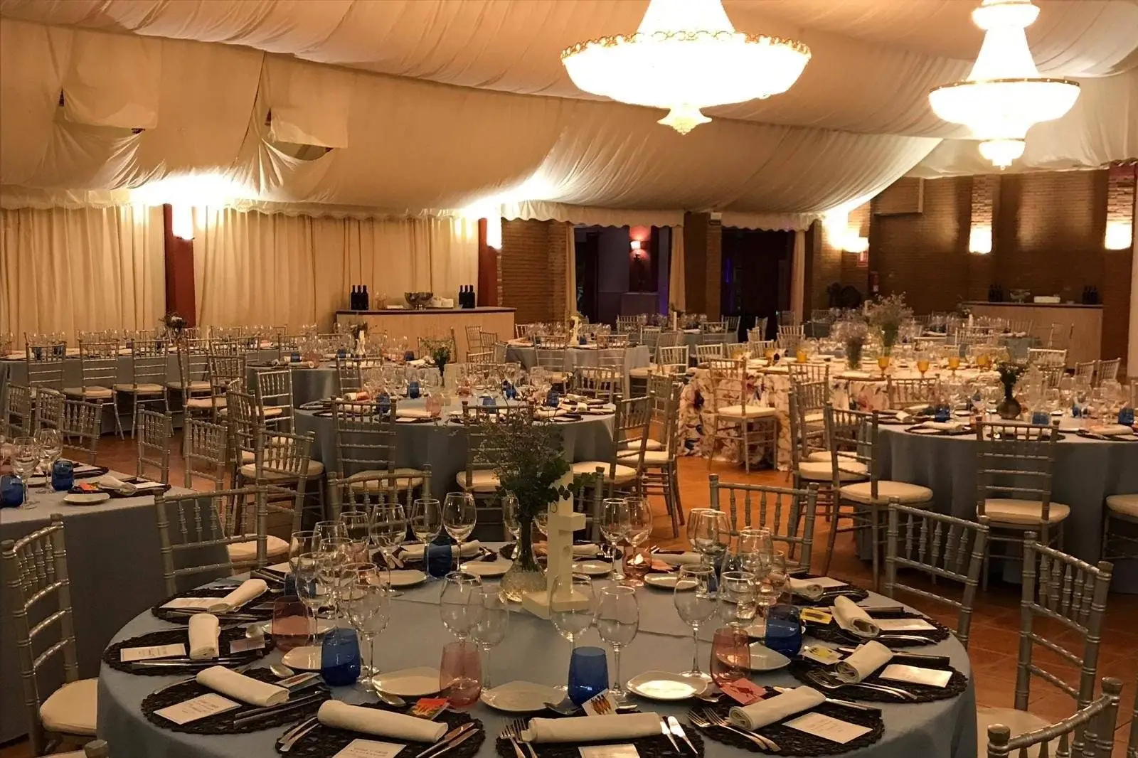 Un salón de banquete con mesas redondas vestidas, sillas de aspas y lámparas de araña bajo un techo de tela blanca